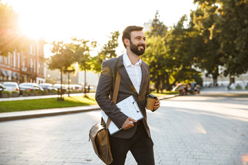 Portrait of beautiful adult businessman in formal suit holding takeaway coffee while walking...
