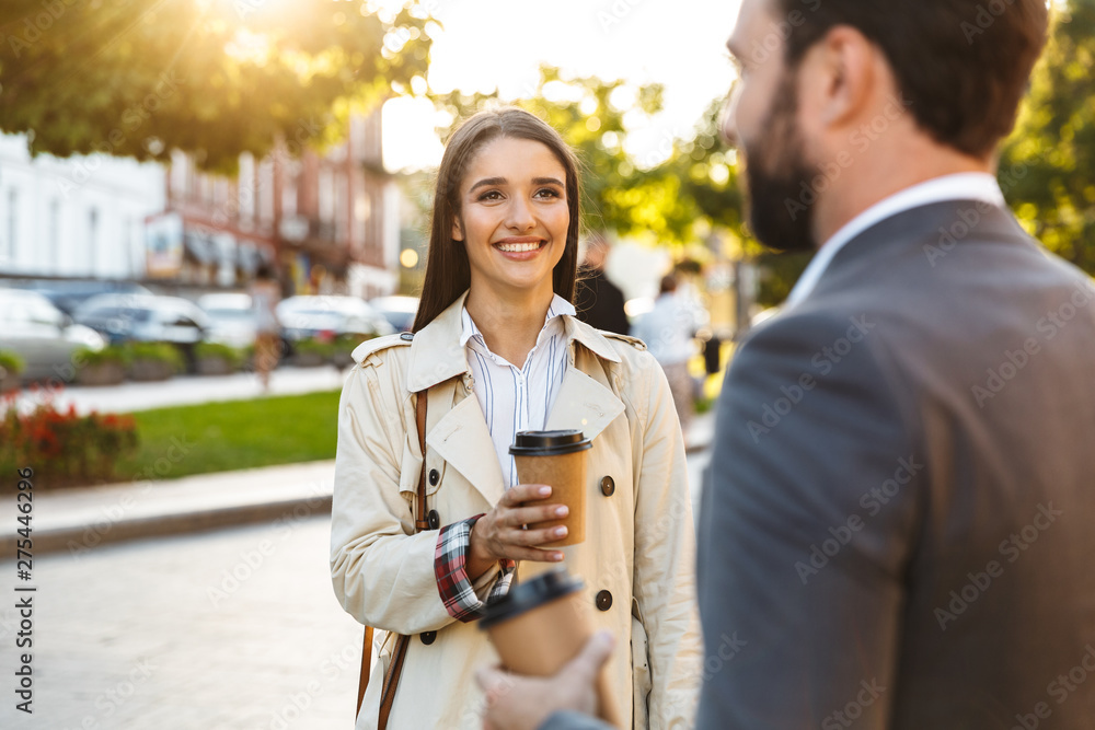 Wall mural photo of pleased office workers man and woman drinking takeaway coffee and looking each other while 