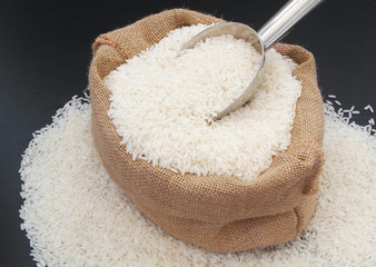 Rice in hessian sack with metallic scoop on black table close up