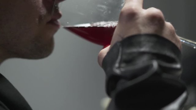 Close-up of confident brutal man in leather jacket drinking red wine from the glass close-up. Alcohol lover resting alone. Studio shot