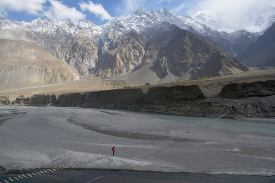 Pakistan, Gilgit Baltista area, Passu, a man is crossing the Hunza river on the Zadabad suspension bridge in front of the Karakoram mountains