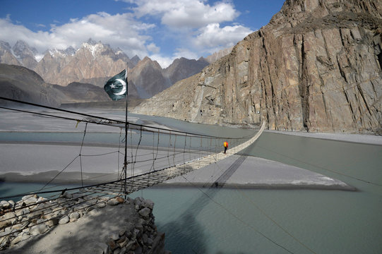 Pakistan, Gilgit Baltistan area, Passu, a man is crossing the Hunza river on the Hosseini suspension bridge in front of the Karakoram mountains