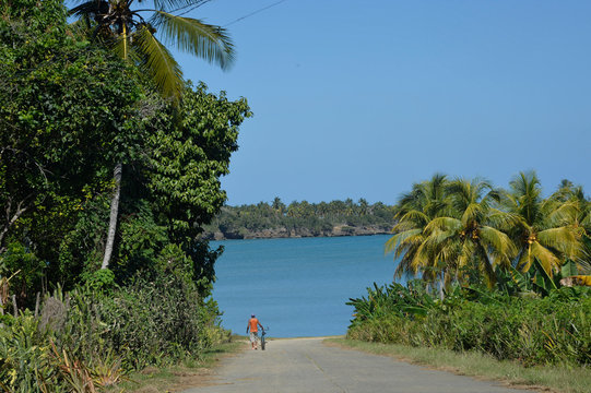 Cuba, Baracoa, Bahia de Mata, a man is walking nearby his bike towards a turquoise blue waters bay