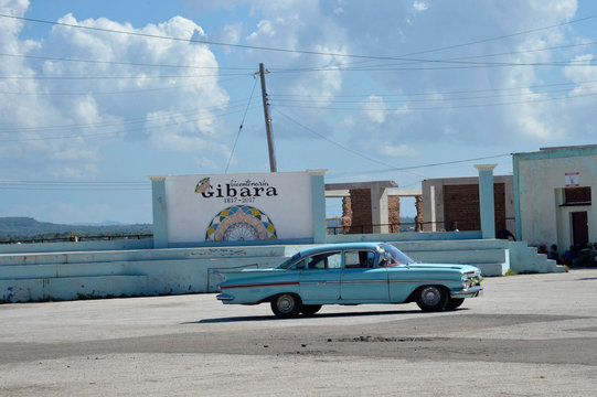 Cuba, Gibara, an old blue 50s American car passes in front of the sign celebrating the bicentennial of the city of Gibara