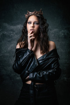 Young woman wearing a crown, a leather jacket, a hand under the chin