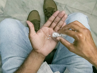 Close-up shot of a man’s hands holding homeopathic pills from the bottle. Medicine and treatment concept.