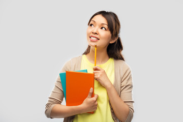 education, high school and knowledge concept - asian student woman with books and pencil over grey background