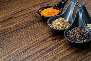 different spices and herbs in spoons or bowls on a brown wooden background . Food and cuisine ingredients with copy space .Dried rosemary,black pepper,red paprika powder or Cayenne Pepper ,oregano
