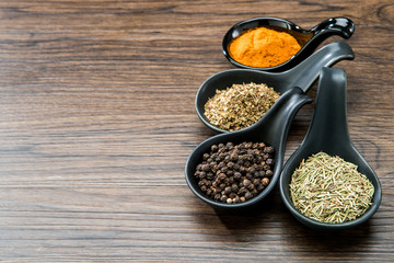 different spices and herbs in spoons or bowls on a brown wooden background . Food and cuisine ingredients with copy space .Dried rosemary,black pepper,red paprika powder or Cayenne Pepper ,oregano
