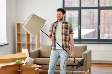 moving, people and real estate concept - happy man with floor lamp at new home - obrazy, fototapety, plakaty