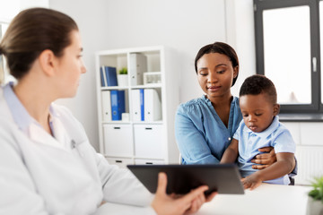 Fototapeta premium medicine, healthcare and pediatry concept - african american mother with baby son and caucasian doctor with tablet computer at clinic