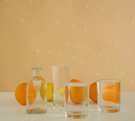 Oranges behind glass vessels filled with water. Distorted reflection on a beige background