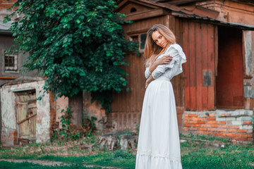 A girl stands alone in a white dress against the background of an old house