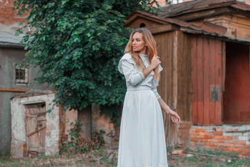 Obraz na płótnie Canvas Beautiful girl on the background of an old house in a white vintage dress