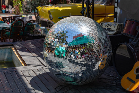 Party over concept. Musical instruments and broken huge disco ball laying on a scene floor against the retro car and other scene decoratios.