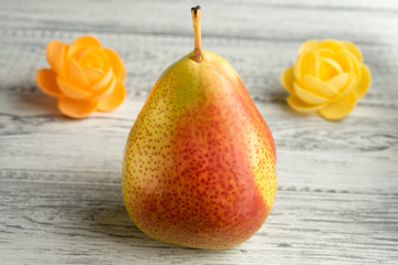 Yellow-red ripe pear on a light wooden background decorated with flowers