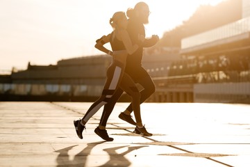 Bearded man with a girl on an evening jog in the open air running along the waterfront illuminated by sunlight