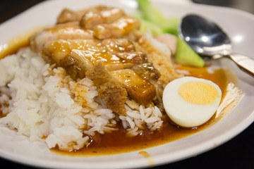 cripsy belly pork with rice and boiled egg close up shot in white dish and cucumber in background