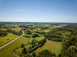 Naklejka premium country road in green forest and fields drone aerial image
