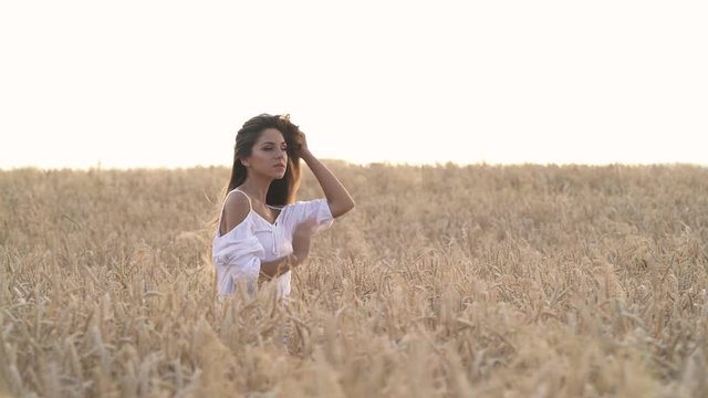 Attractive romantic woman in the wheat field. Wind blowing on her gorgeous brunette wavy hair. Natural beauty concept