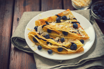 Homemade crepes with blueberries, coconut flakes and chocolate sauce