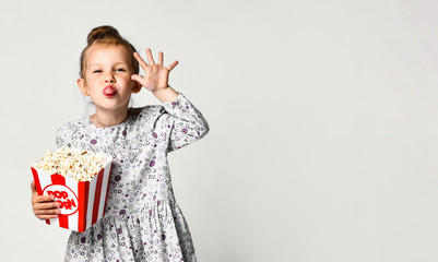 Portrait of a cheery pretty girl holding plastic cup and eating popcorn isolated over white background