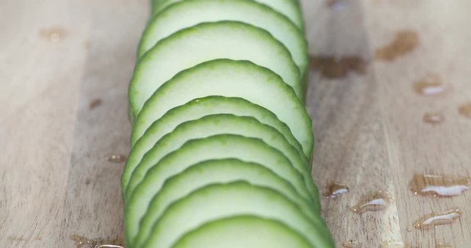 Close-up pan down a row of fresh, ripe slices of English cucumber on a wood cutting board