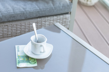 One hundred euro and empty cup of coffee on a glass table of outdoor cafe. Payment, tip.