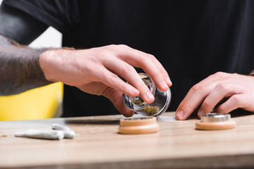 cropped view of man putting medical cannabis on tobacco paper while sitting at table with joints