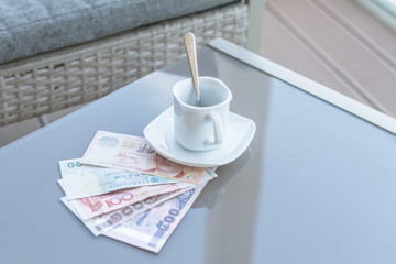 Hong Kong, Indonesia, Malaysia, Thai, Singapore dollar and empty cup of coffee on a glass table of outdoor cafe. Payment, tip.