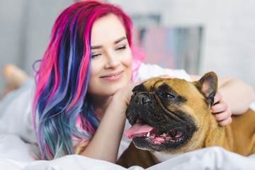 selective focus of french bulldog and girl with colorful hair laying in bed