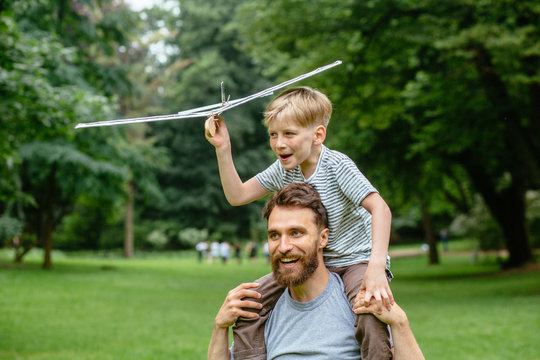My father is the best companion to play with airplane. Beard handsome dad woth son piggyback rides on summer park outdoor. Family happiness holiday vacation activity concept.