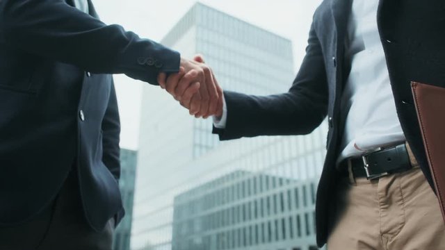 Business people shaking hands with colleague, a handshake on the business center background. Two men in official clothes greeting each other with handshake outdoor.