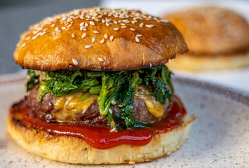 cheeseburger with beef patty, spinach, red sauce, cheddar cheese piled up in a self-made bun