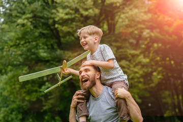 Generation concept. Father giving son ride on back in park. Father and son building together a...