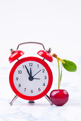 Time for cherry fruits. Red  clock with fresh red cherries on the marble table.