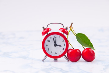 Time for cherry fruits. Red  clock with fresh red cherries on the marble table.