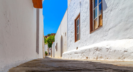 Narrow street in Lindos town on Rhodes island, Dodecanese, Greece. Beautiful scenic old ancient white houses with flowers. Famous tourist destination in Europe