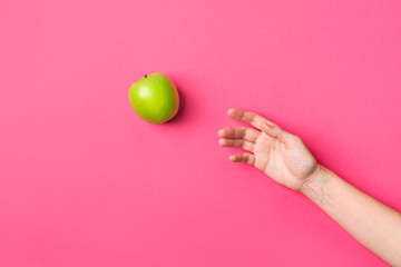 Young Caucasian woman girl reaching for raw green organic apple on fuchsia pink background. Healthy...
