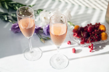 glasses of pink wine on the table next to flowers and fruit