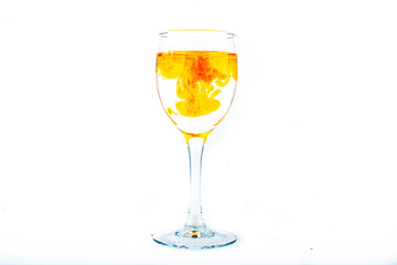 Orange food coloring diffuse in water inside wine glass with empty copyspace area for slogan or advertising text message, over isolated white background.