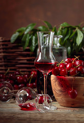 Cherry liquor and red cherries in a wooden bowl on a wooden table in garden.