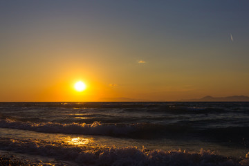Colorful empty seascape with shiny sea over cloudy sky and sun during sunset in Rhodes, Greece