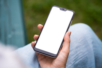 girl with smartphone outdoors in park. Closeup of female hands and smart phone with isolated white screen.
