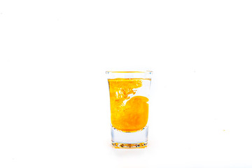 Orange food coloring diffuse in water inside shot glass with empty copyspace area for slogan or advertising text message, over isolated white background.