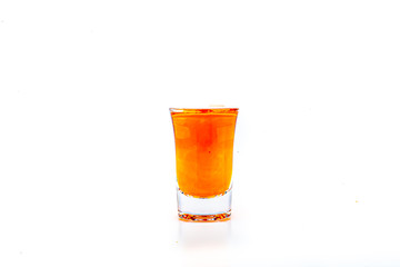 Orange food coloring diffuse in water inside shot glass with empty copyspace area for slogan or advertising text message, over isolated white background.