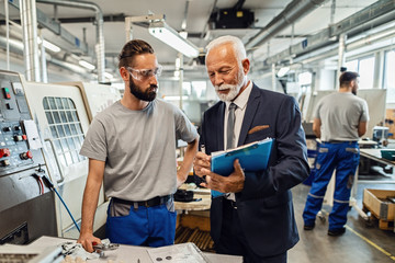 Senior businessman and manual worker reading reports in a factory.