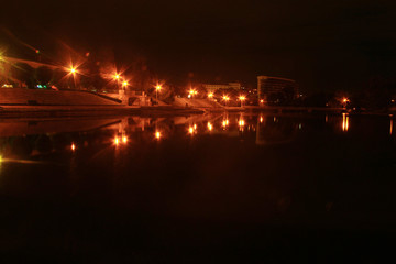 The dark water of the city lake at night reflects the lanterns of orange