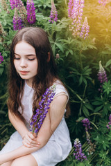 Portrait of young cute brunette girl in lupine violet field in blossom in summer sunset. Greenhouse, nature, natural beauty, freedom, youth concept