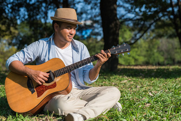 Obraz premium Young asian man playing guitar in park